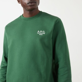 Model wearing A.P.C. dark green cotton sweatshirt with small embroidered white logo on chest.