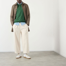 Model wearing A.P.C. dark green sweatshirt, styled with taupe coat, light blue shirt, cream wide-leg trousers and white trainers.