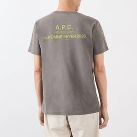 Model wearing grey A.P.C. T-shirt with yellow Automne/Hiver 2026 graphic print on back, styled with beige trousers