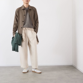 Model wearing taupe button-up jacket and cream wide-leg trousers, styled with a striped top and white shoes, carrying a green bag
