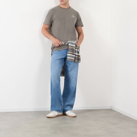 Model wearing A.P.C. T-Shirt in Gris Tahiti, styled with light blue wide-leg jeans and a plaid shirt tied at the waist.