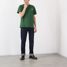 Model wearing A.P.C. dark green cotton T-shirt with small chest logo, styled with dark indigo jeans and black leather shoes.