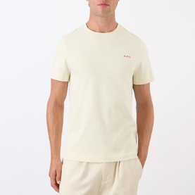 Model wearing A.P.C. Oliver Logo T-Shirt in white, featuring round neck, short sleeves, and small red logo detail on chest, styled with cream