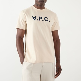 Model wearing A.P.C. T-shirt in mastic with navy blue V.P.C. logo print, styled with light beige trousers.