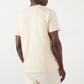 Model wearing A.P.C. mastic cotton T-shirt, rear view, styled with matching mastic trousers.