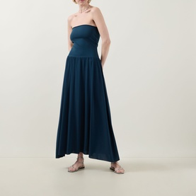 Model wearing Eres Oda Bandeau Dress in Ocean, fitted bodice with full flared midi skirt, styled with gold strappy sandals