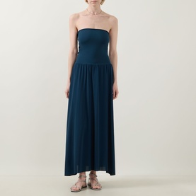 Model wearing Eres Oda Bandeau Dress in ocean teal, with fitted bodice, full flared midi skirt, styled with gold flat sandals.