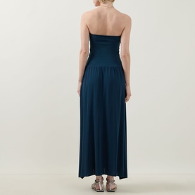 Model wearing Eres Oda Bandeau Dress in Ocean blue, back view, strapless fitted bodice, flared maxi skirt, styled with flat sandals