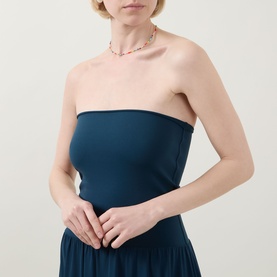 Model wearing Eres Oda Bandeau Dress in ocean blue, showing fitted bandeau bodice and flared skirt, styled with a delicate beaded necklace.