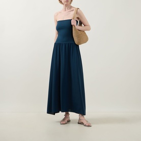 Model wearing Eres Oda Bandeau Dress in Ocean blue, midi length with flared skirt. Styled with woven tote bag and flat sandals.