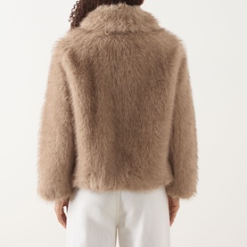Model wearing Max Mara S Malce Faux-Fur Short Coat in Honey, shown from behind with shirt collar and wide fit silhouette, styled with white trousers