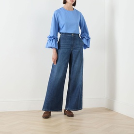 Model wearing Max Mara S China Blue wide-leg jeans in cotton, styled with a blue ruffled-sleeve top and brown loafers.