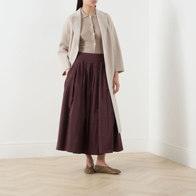 Model wearing Max Mara S Limone Beige Knitted Polo Shirt, styled with a cream coat, burgundy gathered midi skirt and flat shoes.