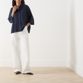 Model wearing Max Mara S Rugiada Chambray Boxy Shirt in Midnight Blue with white wide-leg trousers and black flat shoes.