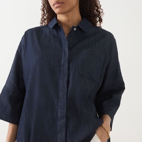 Model wearing Max Mara S Rugiada Chambray Boxy Shirt in Midnight Blue, with cropped sleeves, patch pocket, and wide cuffs. Gold chain necklace