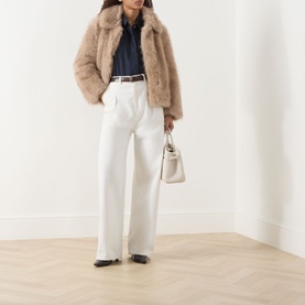 Model wearing Max Mara S Rugiada Midnight Blue chambray boxy shirt, styled with beige faux fur jacket, white wide-leg trousers, and ivory handbag.