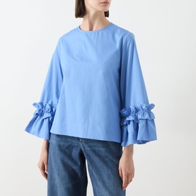 Model wearing Max Mara S light blue cotton shirt with tiered ruffle bell sleeves, styled with blue jeans.