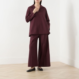 Model wearing burgundy wide-leg trousers and matching oversized collared top, styled with black flat shoes