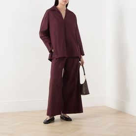Model wearing burgundy wide-leg trousers and matching oversized shirt, styled with a small brown bag and black loafers