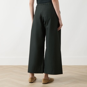 Model wearing Max Mara S green wide-leg cropped cotton trousers with elasticated waist, seen from behind, styled with tan flat mules.