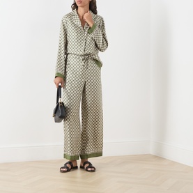 Model wearing Max Mara S Kaki Dice silk trousers with matching printed shirt, styled with black sandals and carrying a small black bag.
