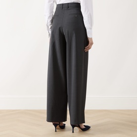 Model wearing Max Mara S Taro High-Waisted Wide Leg Trousers in dark grey wool, styled with a white shirt and navy heels, rear view.