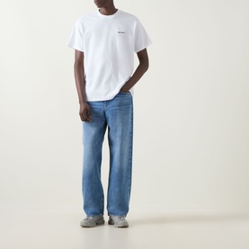 Model wearing Carhartt Script Embroidered Logo T-Shirt in white with blue wide-leg jeans and grey trainers.