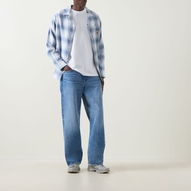 Model wearing Carhartt Script Embroidered Logo T-Shirt in white, styled with blue check overshirt, light wash wide-leg jeans and grey trainers.
