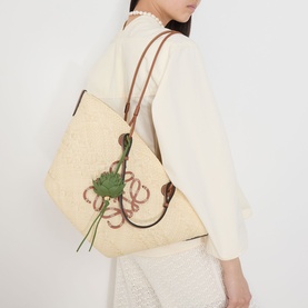 Model with Loewe Artichoke Bag Charm in green, leather strap, artichoke motif, shown attached to a raffia tote bag