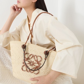 Model carrying Loewe Anagram Medium Basket Bag in natural/black, woven iraca palm with brown leather strap and anagram logo detail.