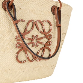 Loewe Anagram Medium Basket Bag in natural, close-up of woven iraca palm body with tan leather Anagram logo appliqu&eacute; and shoulder strap detail