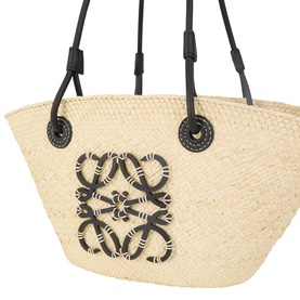Loewe basket bag in natural/black iraca with leather handles, featuring a woven Anagram motif and circular leather hardware detail.