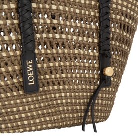 Loewe Braid Medium Basket Bag in khaki and natural woven iraca, close-up showing black leather trim, gold-tone stud and branded tag detail.