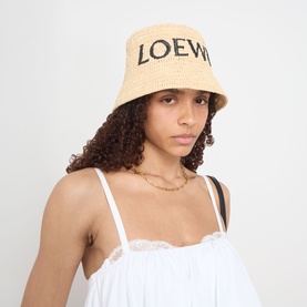 Model wearing Loewe Raffia Logo Bucket Hat in natural, with woven texture and embroidered logo, styled with a white lace cami top.