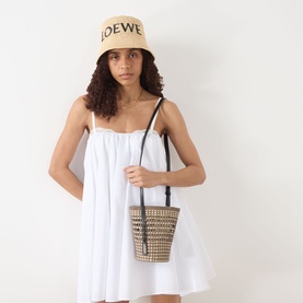 Model carrying Loewe Braid Pocket Crossbody Bag in khaki/natural with black leather strap, styled with white mini dress and Loewe bucket hat.