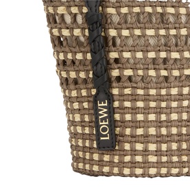 Loewe Braid Pocket Crossbody Bag in khaki and natural iraca, close-up showing woven texture, black leather strap and gold logo tag.