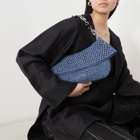 Model carrying Loewe Ola Denim Crochet Medium Shoulder Bag in denim blue with silver chain strap, styled with black oversized coat.