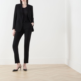 Model wearing Max Mara Studio black blazer with matching black trousers and black heels, full-length view on light wood floor.