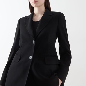 Model wearing Max Mara Studio black blazer with notch lapels, two front buttons and flap pockets, styled over black top.