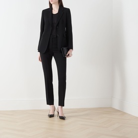 Model wearing Max Mara Studio black blazer with matching black trousers, black top, and black heels, holding a small clutch.