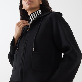 Model wearing Max Mara Studio black wool-silk-cashmere hooded coat, styled with a striped turtleneck underneath, zip fastening visible.