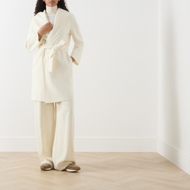 Model wearing Max Mara Studio white wool-silk-cashmere belted wrap coat, styled with wide-leg cream trousers and gold loafers.