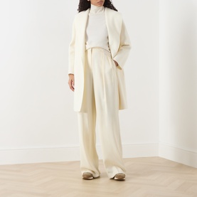 Model wearing Max Mara Studio white wool-silk-cashmere coat, styled with wide-leg cream trousers and a ribbed turtleneck top.