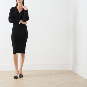 Model wearing Max Mara Studio black ribbed midi dress with white contrast hem trim, V-neckline and long sleeves, styled with black flat shoes.