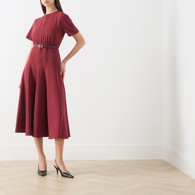 Model wearing Max Mara Studio ruby dress with short sleeves, pleated bodice and flared midi skirt, belted waist, styled with black slingback heels.