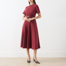 Model wearing Max Mara Studio ruby dress with short sleeves, pleated bodice, belted waist and full midi skirt, styled with black heels.
