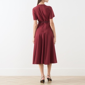 Model wearing Max Mara Studio ruby dress, rear view, short sleeves, belted waist, flared midi skirt, styled with black heels.