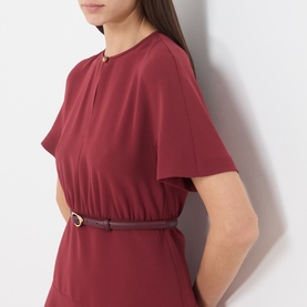 Model wearing Max Mara Studio ruby dress with short sleeves, elasticated waist, gold keyhole neckline detail, styled with a thin belt.