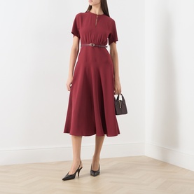 Model wearing Max Mara Studio ruby dress with short sleeves, cinched belt waist and midi flared skirt, styled with black heels and small bag