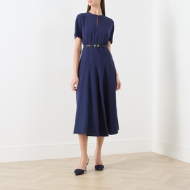 Model wearing Max Mara Studio navy dress with short sleeves, keyhole neckline, belted waist and midi flared skirt, styled with navy flats.